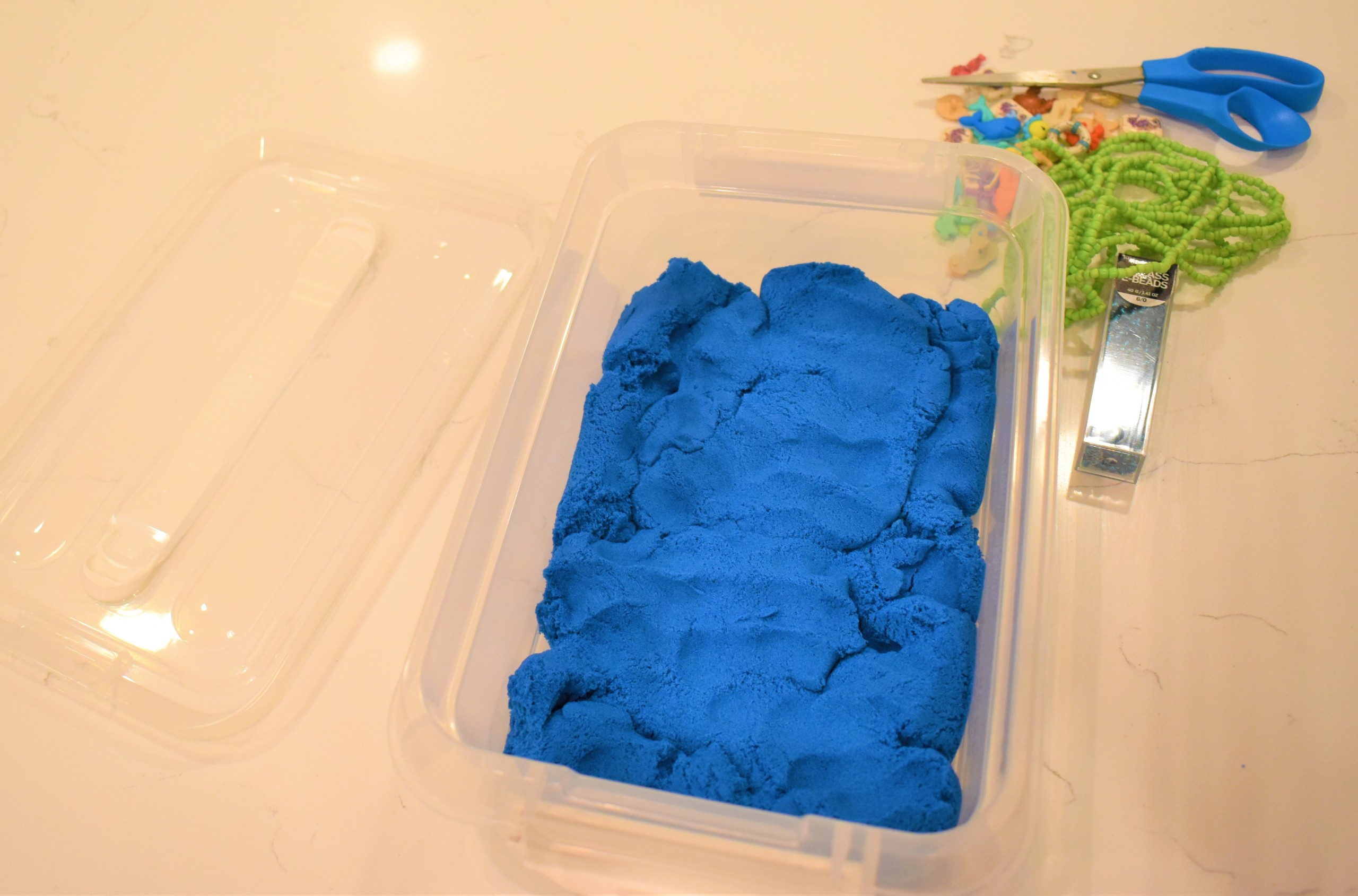 Blue Kinetic sand in a plastic bin.