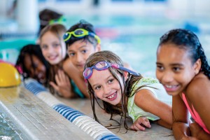 Children are smiling by the edge of a pool.