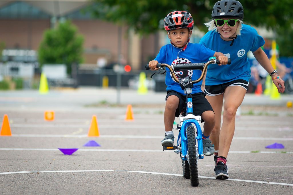 An instructor walks behind a child who is learning to ride a bike.