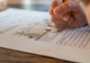Stock photo of a child's hand gripping a pencil and completing a worksheet on a table.