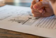 Stock photo of a child's hand gripping a pencil and completing a worksheet on a table.