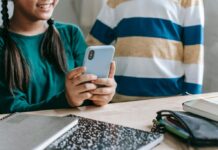 Stock photo of a tween girl smiling as she uses a cell phone at a table.