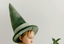 Stock photo of a girl dressed in a pointy green hat and a matching cloak. There is a green leafy plant curling up in the foreground.