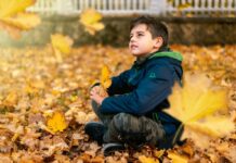Where To See Fall Foliage in November: Philly and Southeast U.S. Child sitting thoughtfully among bright yellow fall leaves