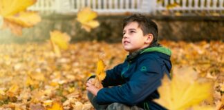 Child sitting thoughtfully among bright yellow fall leaves