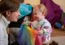 A mother and baby playing with a rainbow scarf
