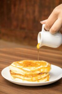 Person pouring syrup on a stack of pancakes