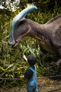 A child reaches up towards a dinosaur statue