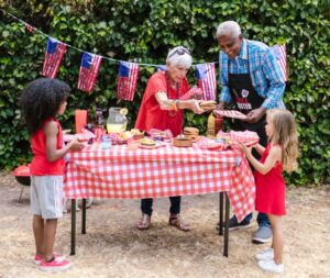 Kids being served food at a Fourth of July barbecue by an elderly man and woman