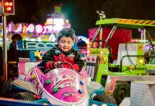 2026 Carnivals & Fairs: Philadelphia and the Delaware Valley A boy sits in a pink ride car at a carnival at night with bright lights surrounding him in the background.